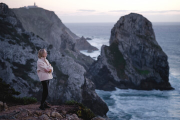 A woman stands on the rocks on the backdrop of Cape Roca, Sintra, Portugal.