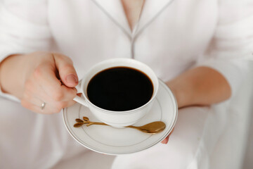 Cozy woman in pajamas holding a cup of hot coffee while relaxing at home