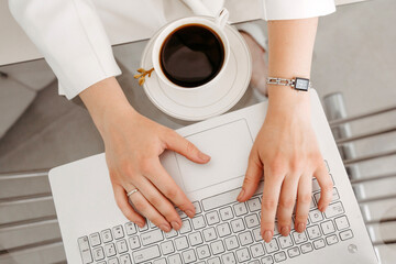 Female hands work on a modern laptop. Next to a cup of coffee