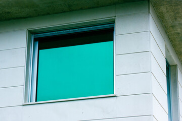 External view of blue glass window. A corner of a residential building, facade of a white house, villa, hotel. Architectural details of the exterior, modern structure. Mirrored green windows.