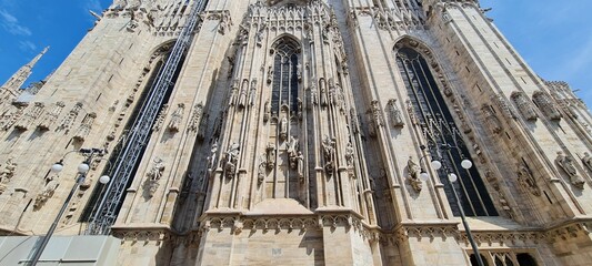 Naklejka premium Cathedral Duomo di Milano. Panoramic view of the ornate facade with many marble sculptures on the wall. Entrance to the cathedral of European country. Detail of a building.