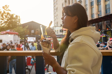 woman eating Belgian french fries with sauce at food court. street food festival on background blurred