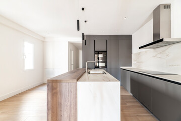 Minimalist kitchen with gray furniture without handles and an island with a stainless steel sink on white marble