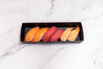 Black home delivery tray with six pieces of nigiri sushi of different fish