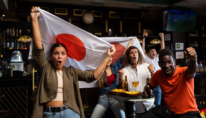 Excited young woman, Japan football team fan, spending time in bar with friends while watching...