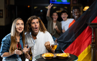 Man and woman, Germany football team fans, spending time in bar, drinking bear and screaming chants. People with state flag in pub.