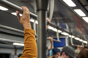 man holding on to the safety bar of a crowded train car at night. Public transport interior