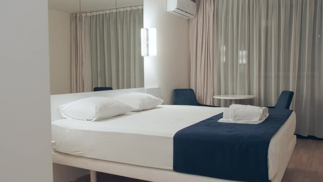 Interior of room in privat hotel with large queen size bed, table, blue armchairs, mirror and air conditioner. Empty room ready for guests to check in. Lifestyle for businessman on business trips.