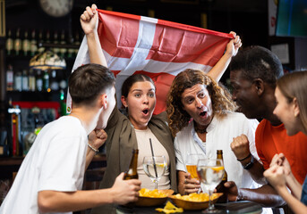 Excited multiracial soccer fans with flag of Switzerland celebrating victory of team with pint of...