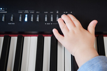 Toddler baby plays piano in home living room, music lessons. Happy child boy learns to play music on an electric piano. Kid boy age one year four months