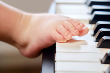 Toddler baby foot on electric piano keys, close-up. Child feet lie on an electronic portable piano....