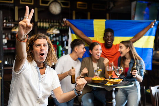Cheerful proud football fan gesturing emotionally after goal scored by favorite team while watching championship match on TV in sports bar 