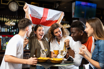Group of England football team fans spending time in bar, drinking bear and having fun. People with state flag in pub. - obrazy, fototapety, plakaty