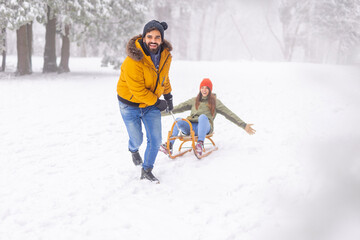 Man pulling woman on sledge while on winter vacation