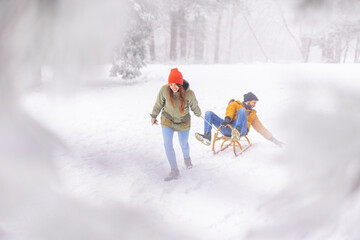 Fototapeta na wymiar Woman pulling man on sledge while on winter vacation