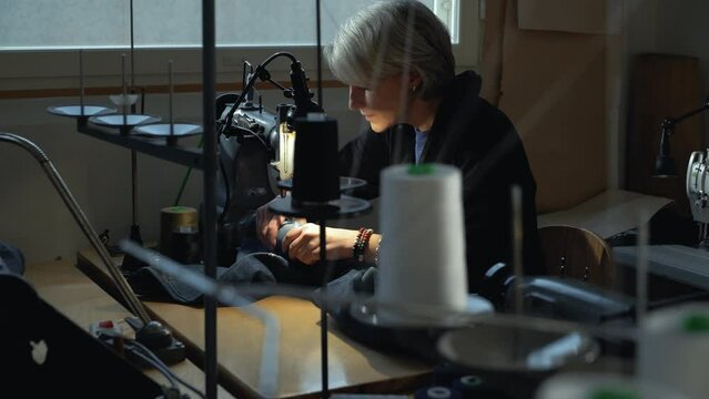 A female tailor seamstress repair old jeans with vintage darning machine in a workshop repairing denim clothes. Small family business, tailoring and repair of clothes, handmade, startup.