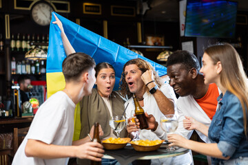 Happy emotional people of different ages and nationalities waving national flag of Ukraine while...