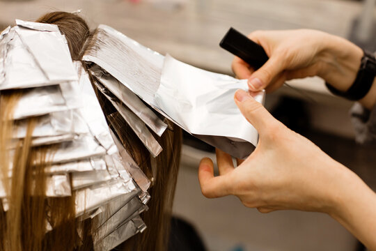 Hairdresser is dyeing female hair, making hair highlights to his client with a foil.