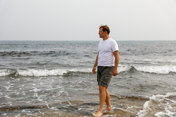 Fototapeta na wymiar A young handsome man walks by the sea, the concept of a healthy lifestyle