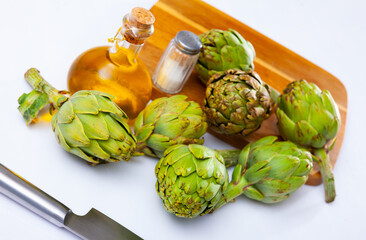 Fototapeta premium Bunch of artichokes placed over white background with saltcellar and glass oil bottle.