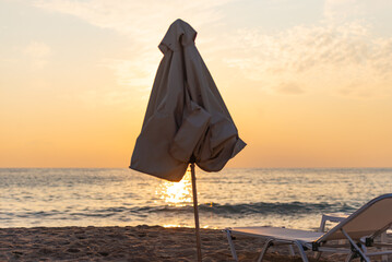Sun lounger and umbrella on the background of the sunset sea. Folded beach umbrella covers the sun.