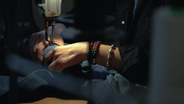A female tailor seamstress repair old jeans with vintage darning machine in a workshop repairing denim clothes. Small family business, tailoring and repair of clothes, handmade, startup. Close-up