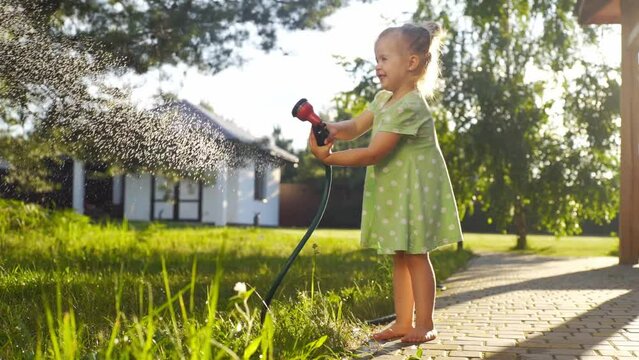 A little girl waters the lawn with a hose