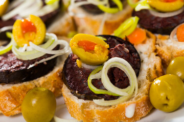 Image of tasty canapes from blood sausage with bread and olives, served at plate