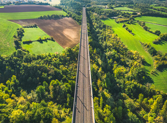 Aerial view of the railroad tracks for high-speed trains on the flyover. Panoramic autumn view of the surrounding fields and forests and the surrounding mountains.