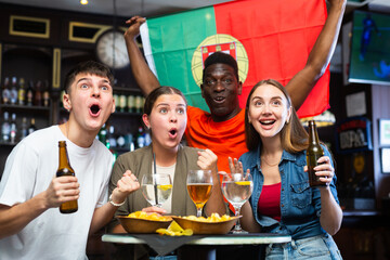 Excited young adult football fans having fun in sports bar, celebrating victory of favorite...