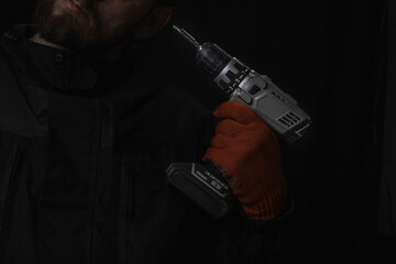 Hand holds cordless electric screwdriver with bit for screws and drilling isolated on black...