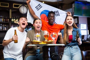 Diverse men and women supporting South Korea sports team in pub together. Happy group of friends...