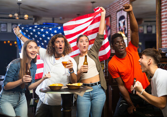 Group of emotional young adults, American football fans cheering for favorite team together in...