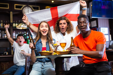 Happy international sport supporters holding up the flag of England and drinking beer in the pub