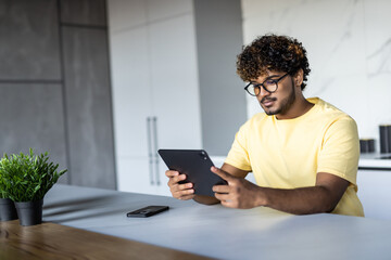 Indian man using digital tablet white sitting in the kitchen