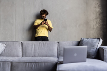 Young indian man sitting on sofa and scrolling news phone at home