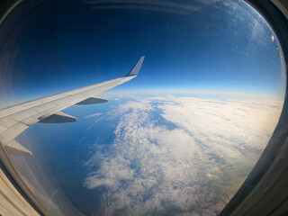 view of the clouds and the wing of an airplane from the window on a sunny day