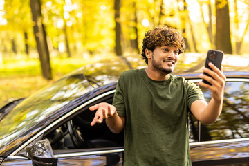 Young indian man standing near his car and make video call on the phone