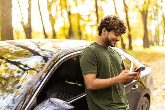 Successful indian man standing by his car texting on mobile phone