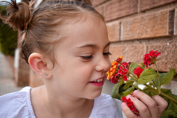 Naklejka premium Niña pequeña rubia oliendo flores de colores vivos