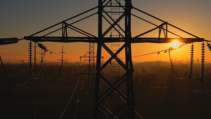 High voltage electric towers at golden hour sunset. Transmission power line and grid infrastructure. Power line insulators and wires silhouette. Energy crisis and high gas and oil prices concept.