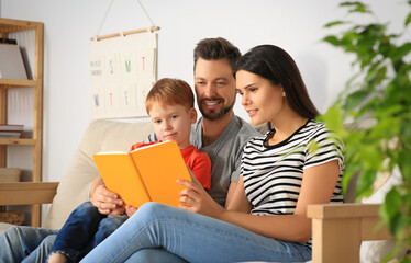 Fototapeta premium Happy family reading book together on sofa in living room at home