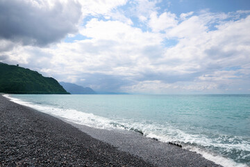 Picturesque view of beautiful sea shore and mountains under sky with fluffy clouds