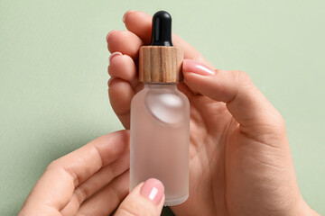 Woman holding bottle with serum against olive background, closeup