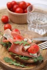 Tasty bruschetta with prosciutto, arugula, cheese and tomato on wooden board