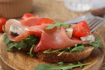 Tasty bruschetta with prosciutto, arugula, cheese and tomato on wooden board, closeup