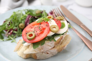 Tasty bruschetta with tomatoes, mozzarella and olives on plate, closeup
