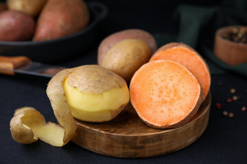 Wooden board with fresh potatoes on black table
