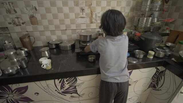 Handheld shot of little Asian girl boiling milk in the kitchen, from the back and side angle