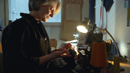 A female tailor seamstress hemming old jeans with vintage authentic machine in in a workshop repairing old denim clothes. Small family business, tailoring and repair of clothes, handmade, startup.
